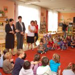 Kanclerz, wicekanclerz i dyrektor przedszkola wśród siedzących na dywanie dzieci w sali zabaw