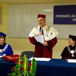 Rektor prof. Michał Woźniak z mikrofonem, obok przy stole prezydialnym siedzą dziekan dr Jolanta Stanienda i kanclerz mgr Zofia Kozioł