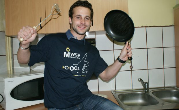 Student siedzący na ladzie kuchennej i trzymający w ręce patelnię