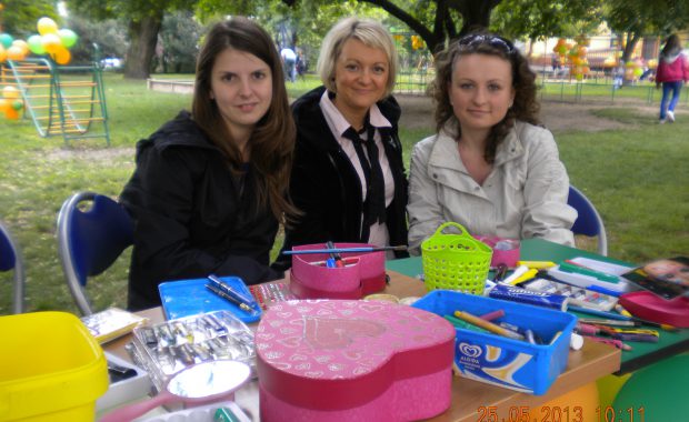 Trzy studentki pedagogiki siedzące przy stoliku w ogrodzie przedszkola, na stole przygotowane przybory do malowania twarzy