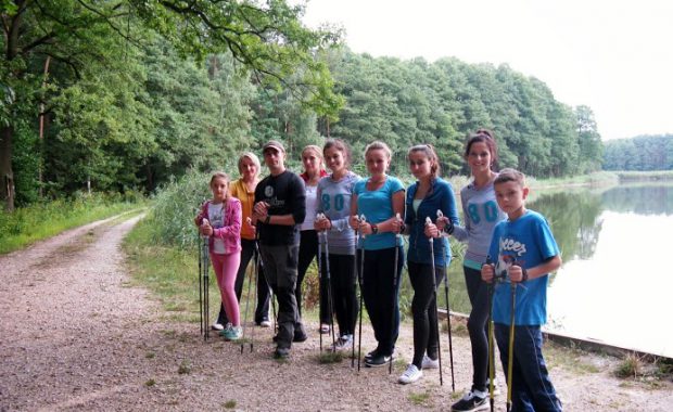 Grupa studentów podczas przerwy w marszu stoi na brzegu jeziorka