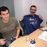 Dwóch studentów z Turcji siedzi przy biurku, jeden z nich trzyma koszulkę z logo Uczelni