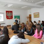 Uczniowie szkół średnich siędzący przy stołach w sali konferencyjnej. W tle mgr Karolina Chrabąszcz prowadzi prelekcję