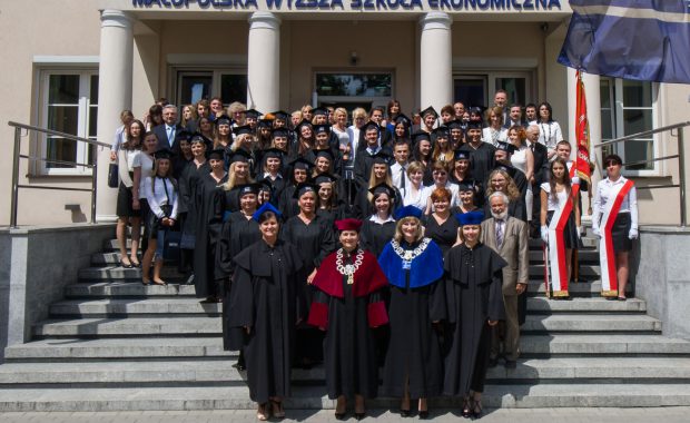 Zdjęcie grupowe władz Uczelni i Absolwentów w tradycyjnych biretach i togach. Grupa stoi na schodach przed budynkiem MWSE przy ul. Waryńskiego 14