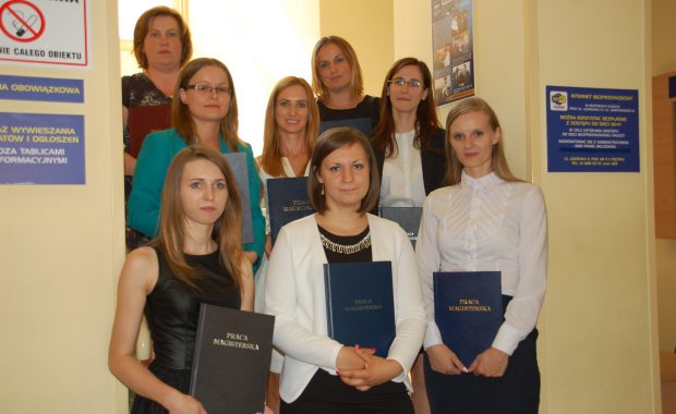 Zdjęcie grupowe studentek - stoją na schodach w 3 rzędach przed sobą trzymają prace dyplomowe