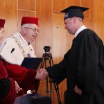 Rektor i Kanclerz wręczają dyplom studentowi
