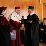 Rektor i Kanclerz wręczają dyplom studentowi