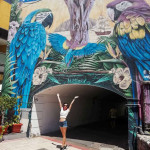 Studentka pozuje na tle przejścia z muralem przedstawiającym papugi