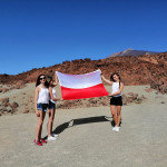 Trzy studentki trzymające rozłożoną polską flagę, w tle skały