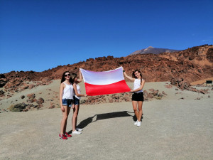Trzy studentki trzymające rozłożoną polską flagę, w tle skały
